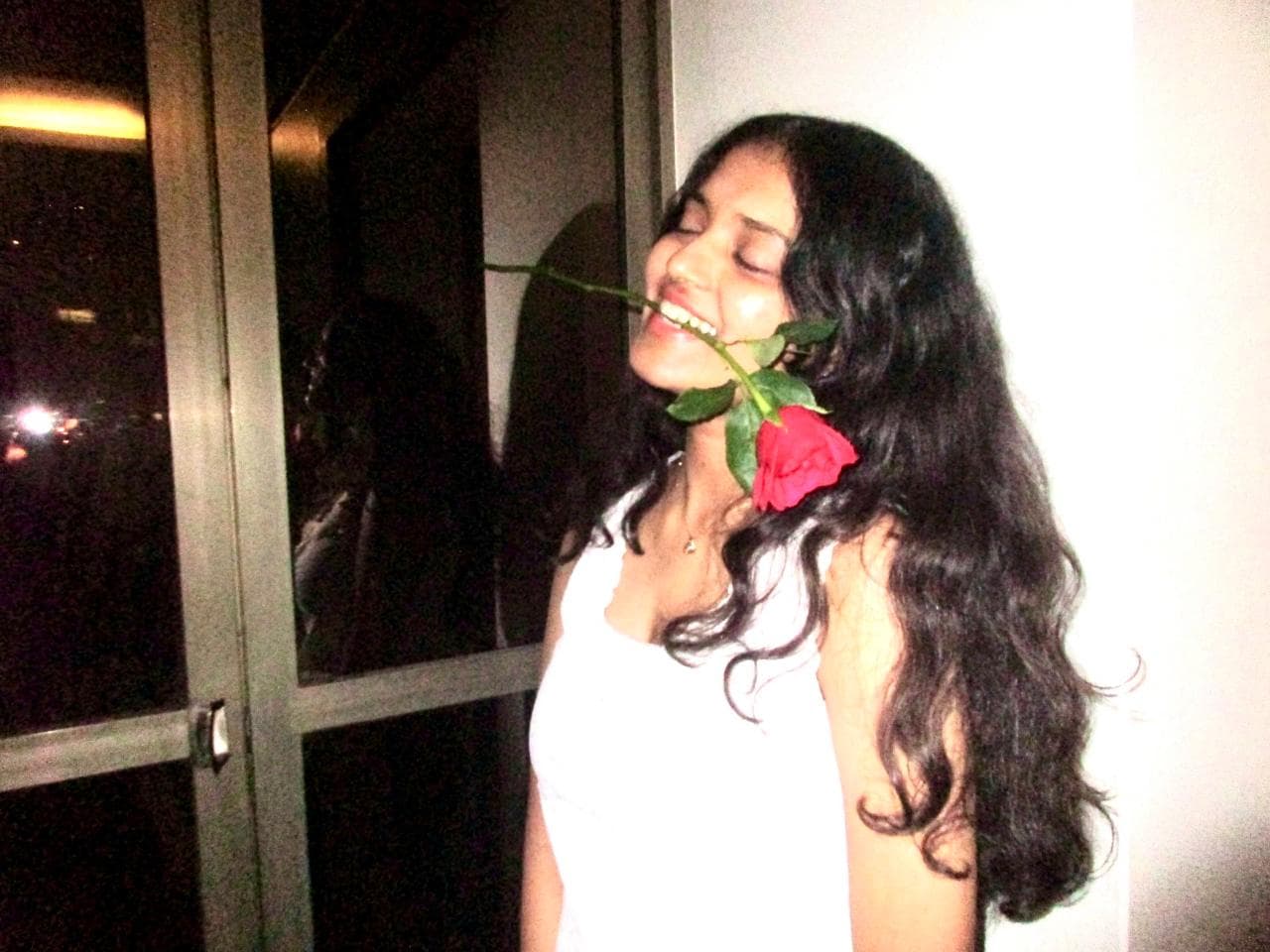 Sara laughing, a red rose held in her teeth