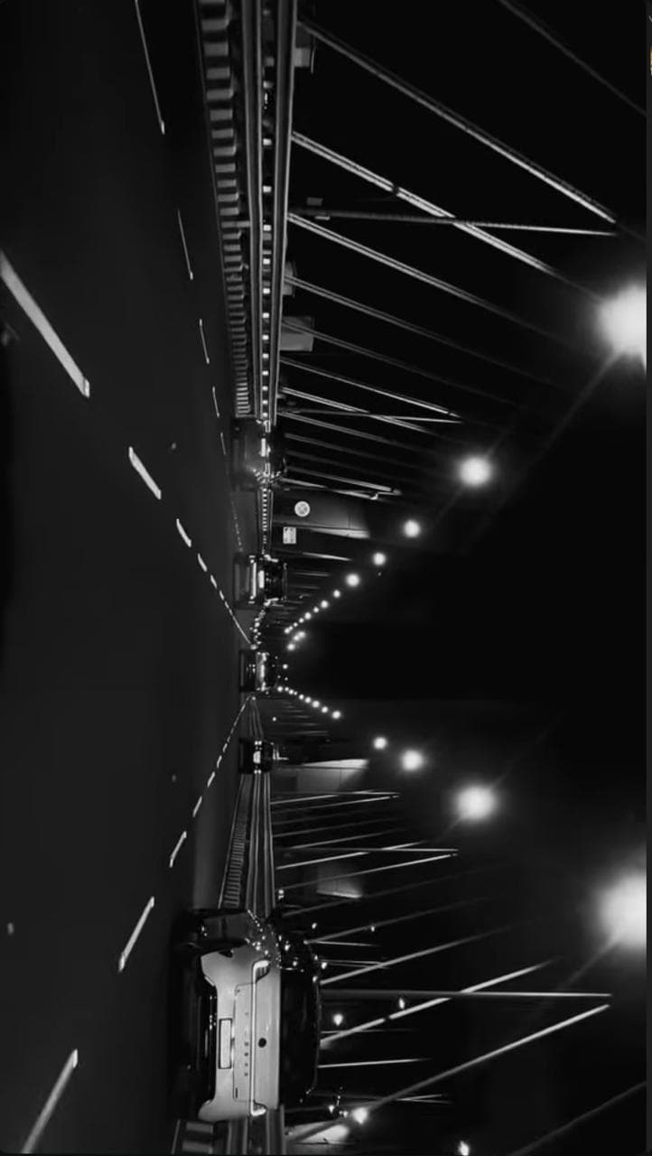 A road at night beneath bridge lights, in black and white